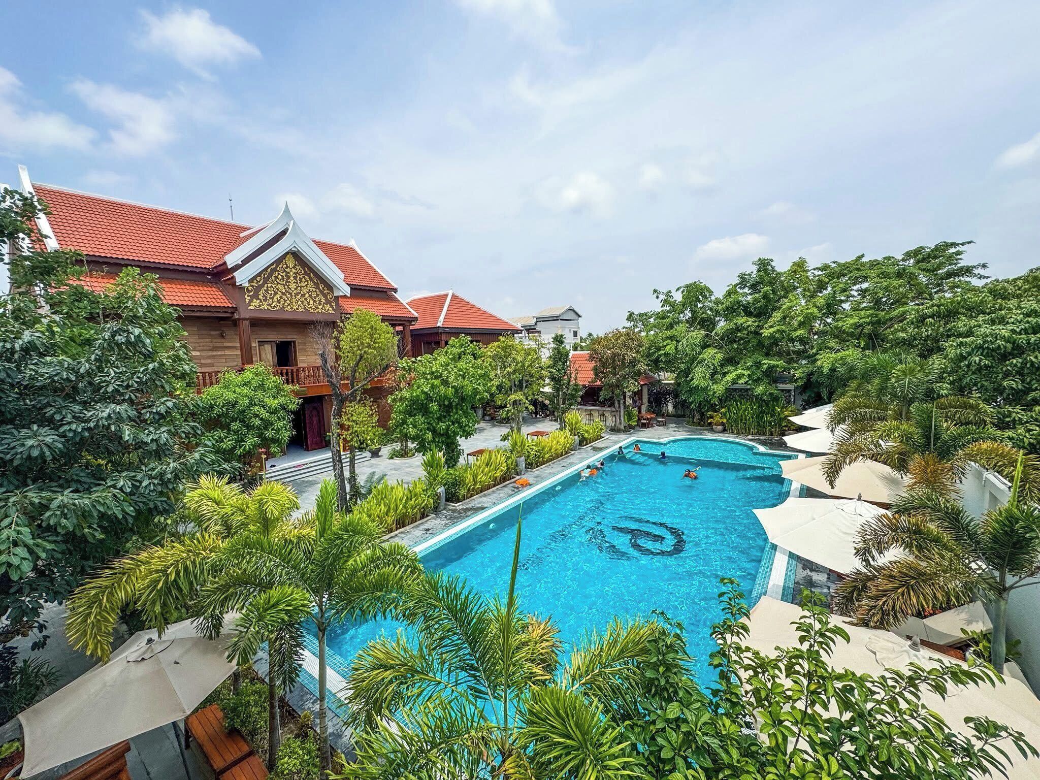 A swimming pool surrounded by lush greenery and traditional buildings with red roofs.