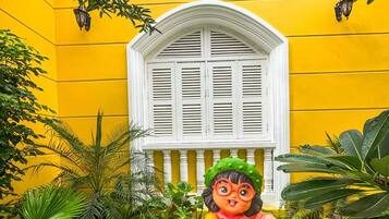A statue of a child holding a basket of fruit in front of a yellow building with a white window and balcony.