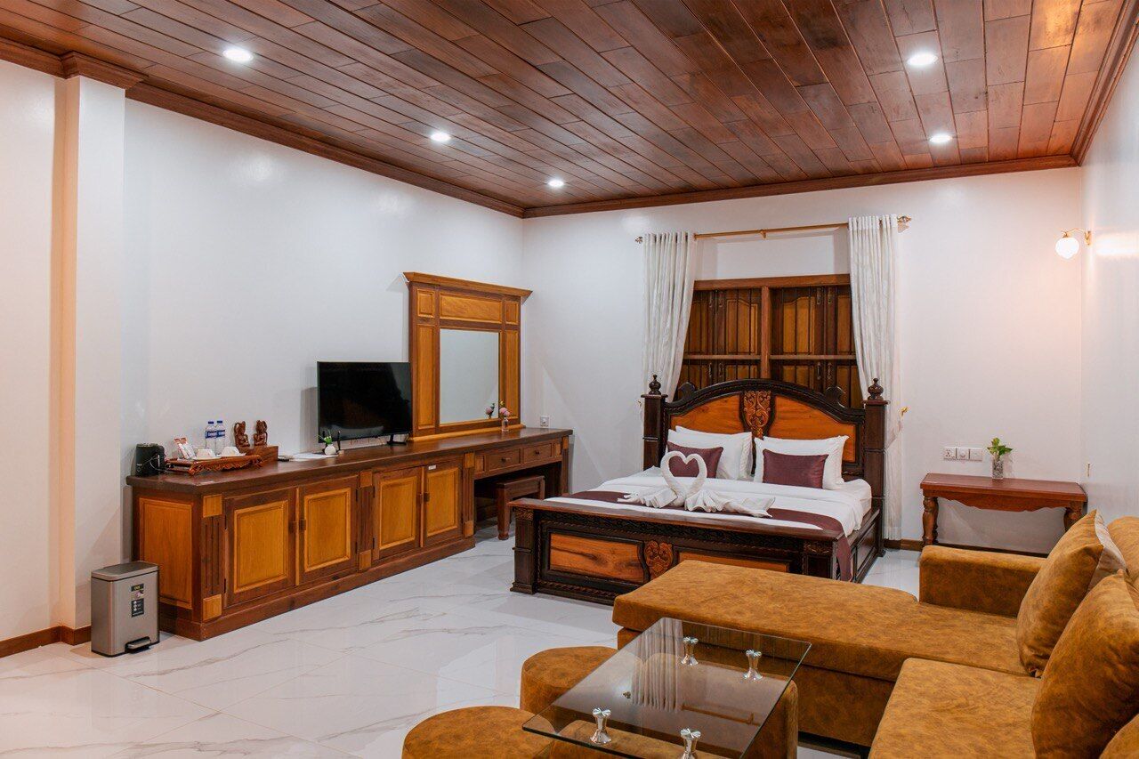 A bedroom with a wooden headboard, a large mirror, a TV, a wooden dresser, and a sofa.