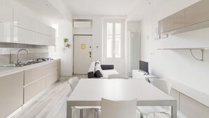 A modern kitchen with white cabinetry, a dining area with a white table and chairs, and a visible door leading to another room. - GuestHost - MM5 Isola Bright Apartment (Milano)