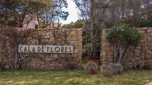 A stone wall with a sign reading 'CALA DE FLORES' surrounded by greenery and trees.