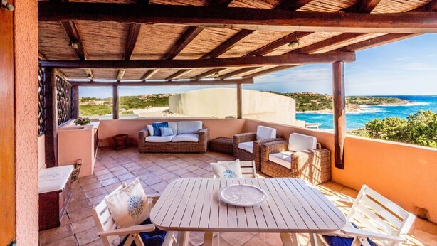 A covered outdoor area with a table and chairs, a sofa, and a view of the ocean.