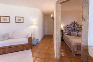 Une pièce avec un canapé blanc, un lit doté d’une tête de lit décorative, une lampe et deux tableaux encadrés accrochés au mur.