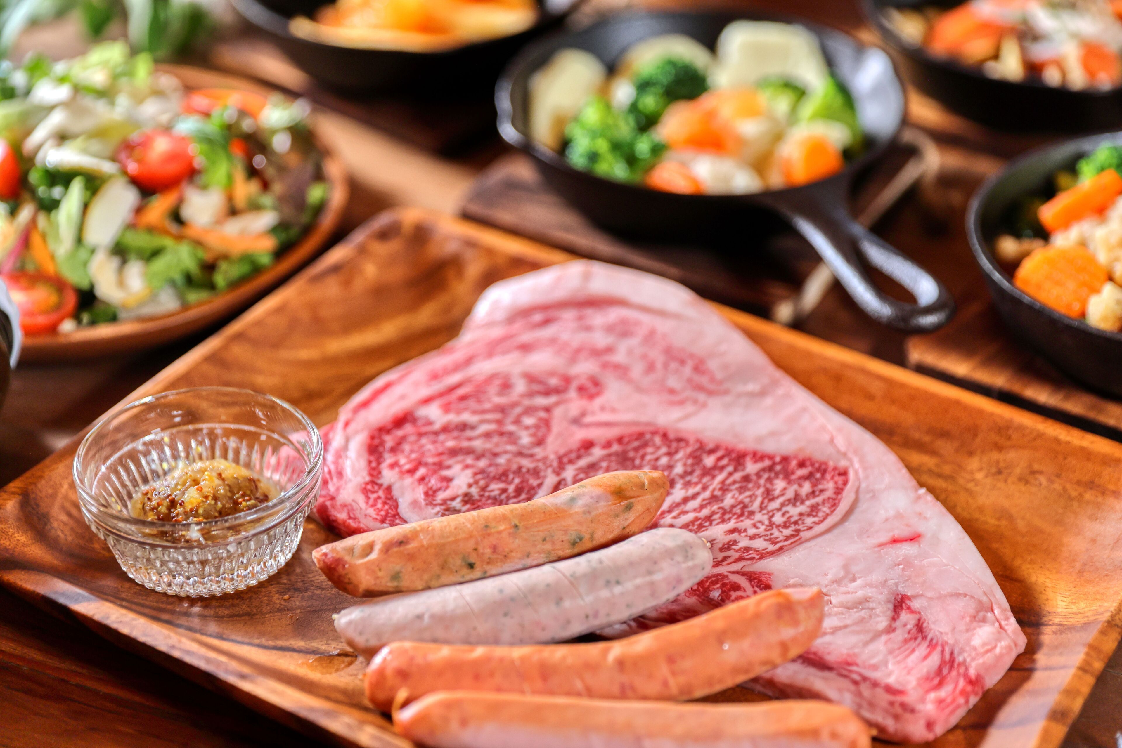 Une planche à découper en bois sur laquelle on trouve de la viande crue, des saucisses et un petit bol d’épices.