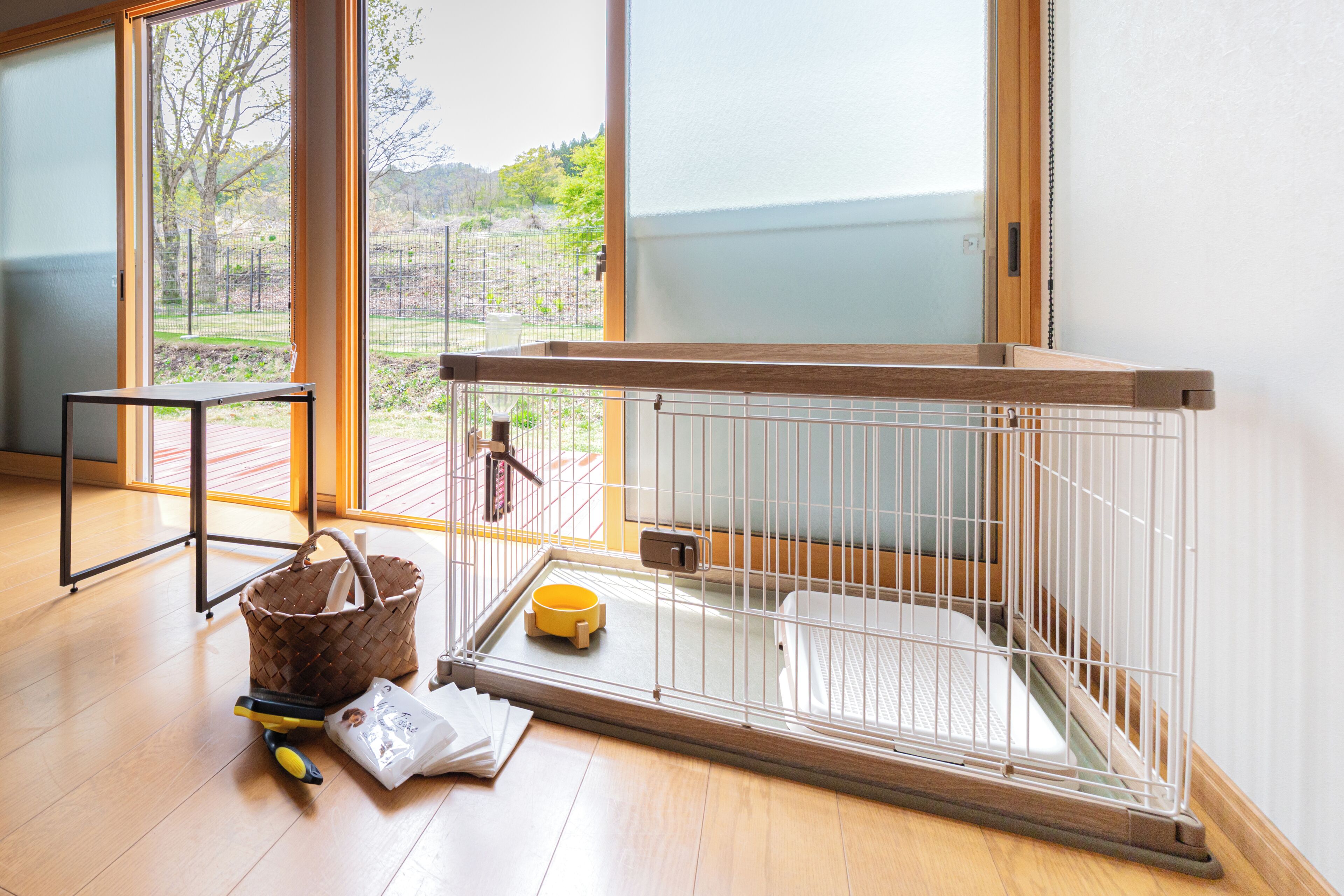 A room with a wooden floor, a metal cage, a basket, and a window with a view of greenery.