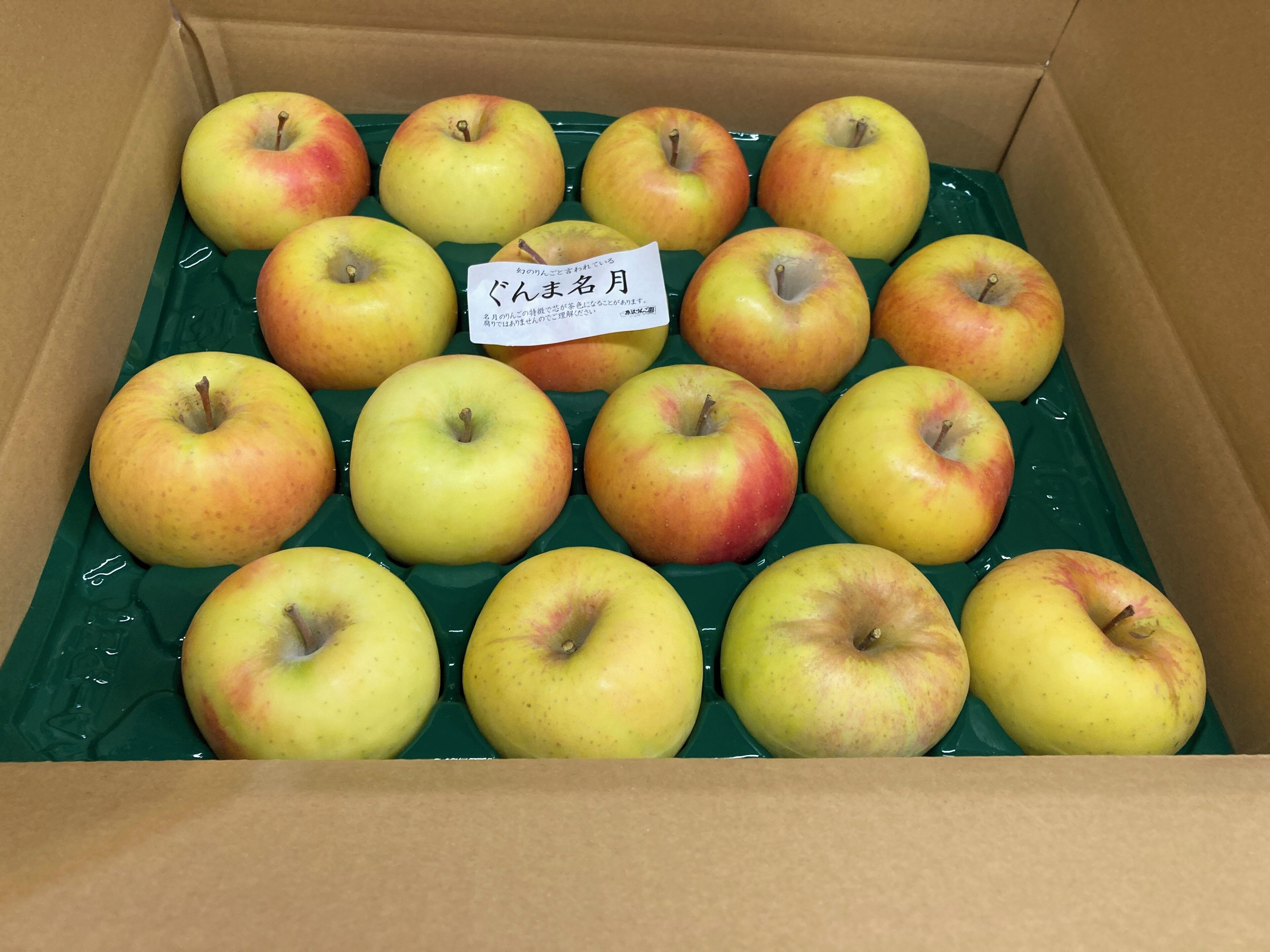 Una caja de cartón con bandejas de plástico verde y manzanas amarillas.