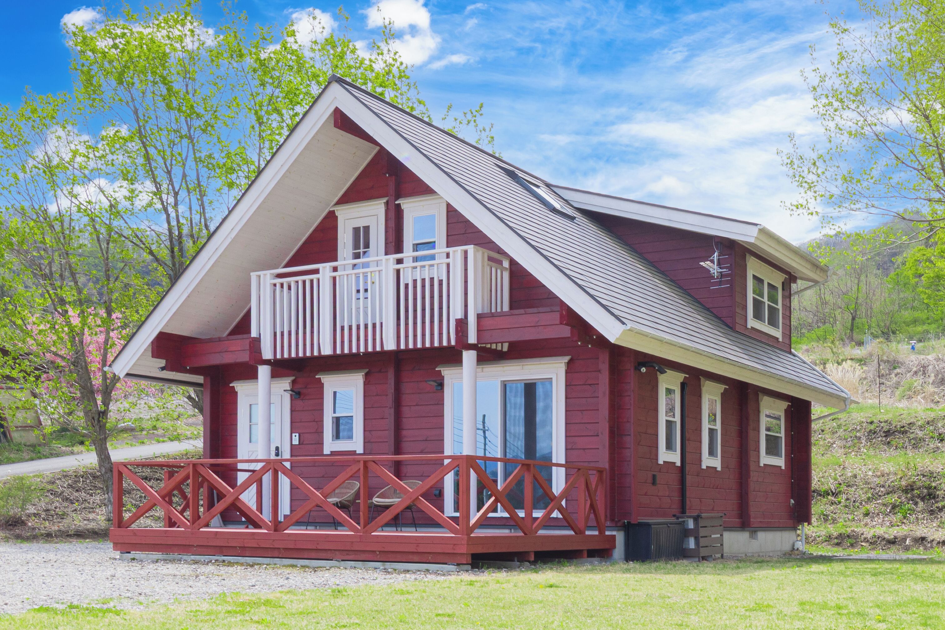 A two-story red wooden house with a balcony, a porch, and a small front yard.