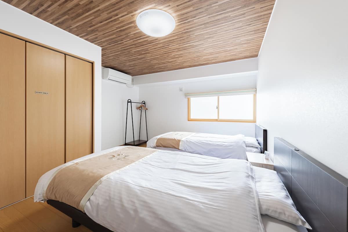 A hotel room with two beds, a wardrobe, a wardrobe with a 'staff only' sign, a window, and a ceiling with wooden panels.