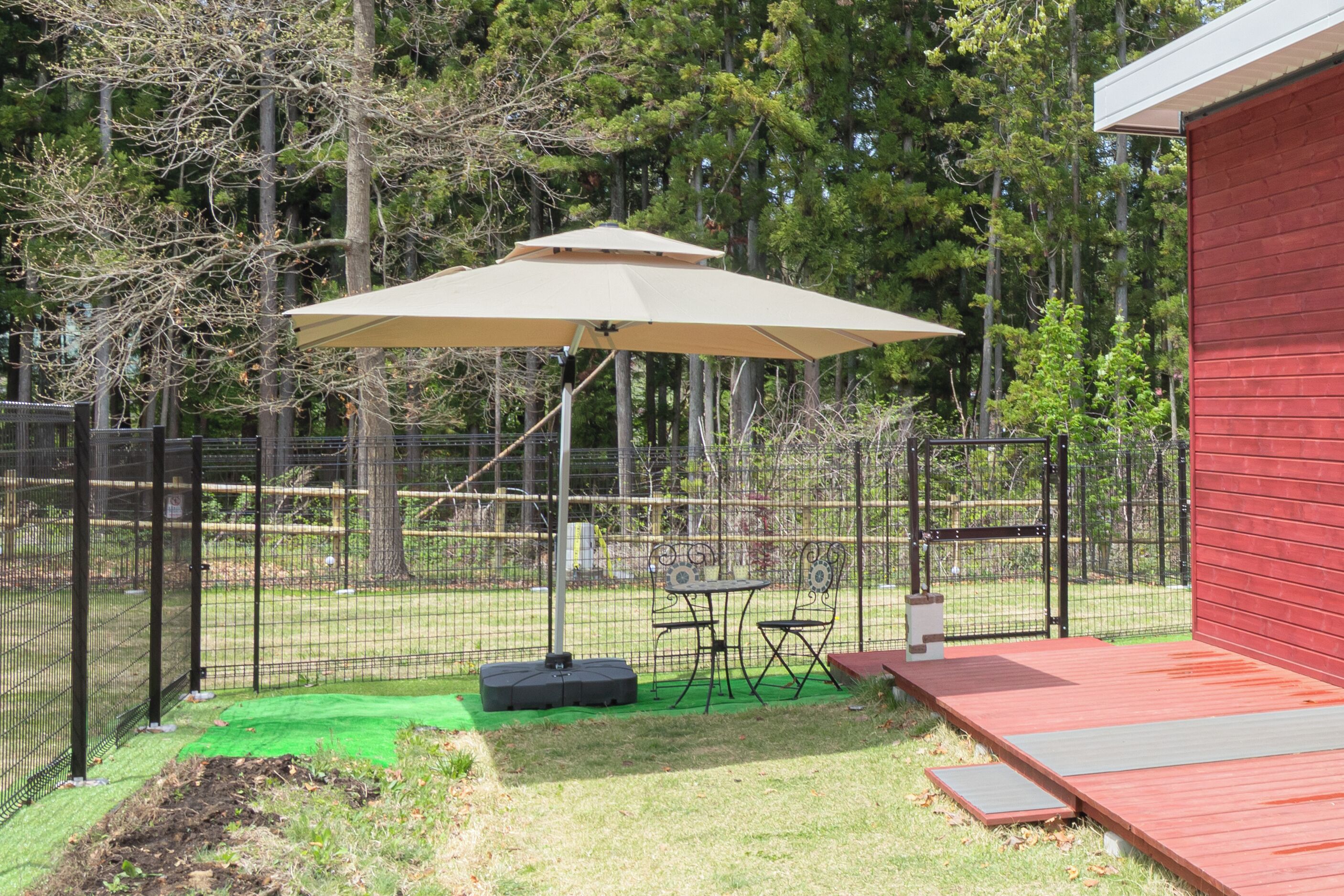 A fenced backyard with a table and chairs, a stage, and a red building.