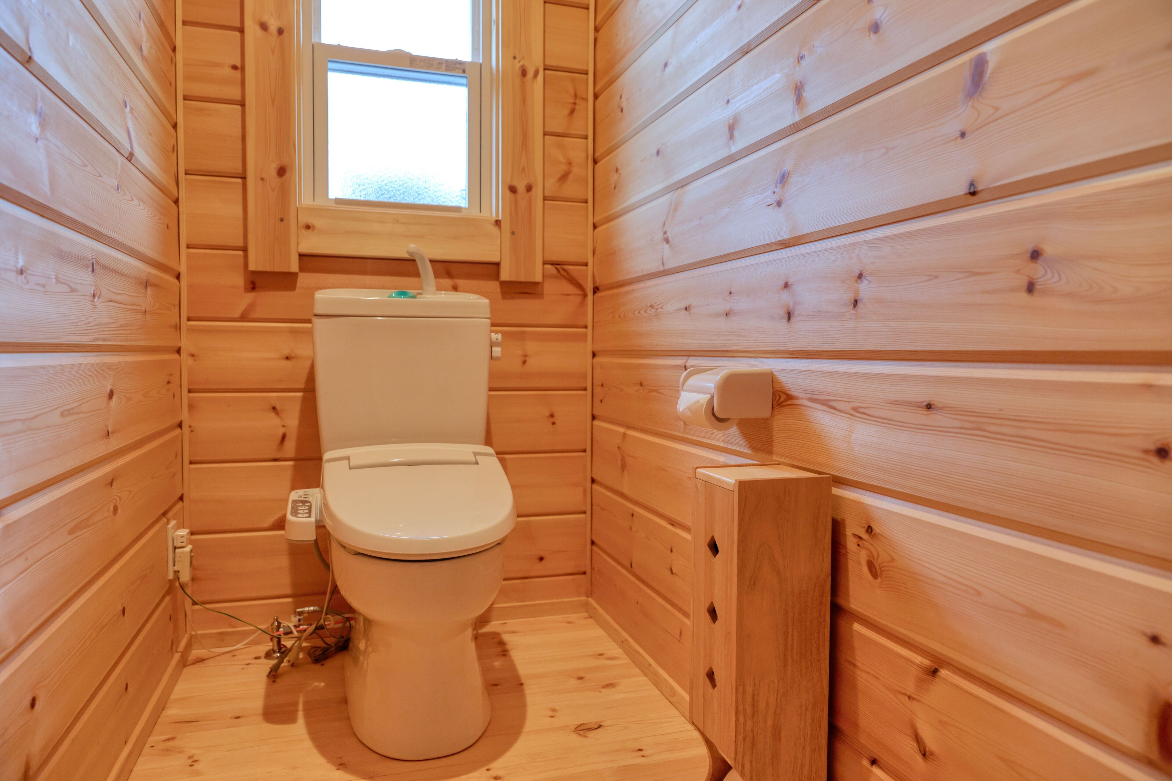 Un baño pequeño con paneles de madera, un inodoro, un ventanal y un armario de madera.