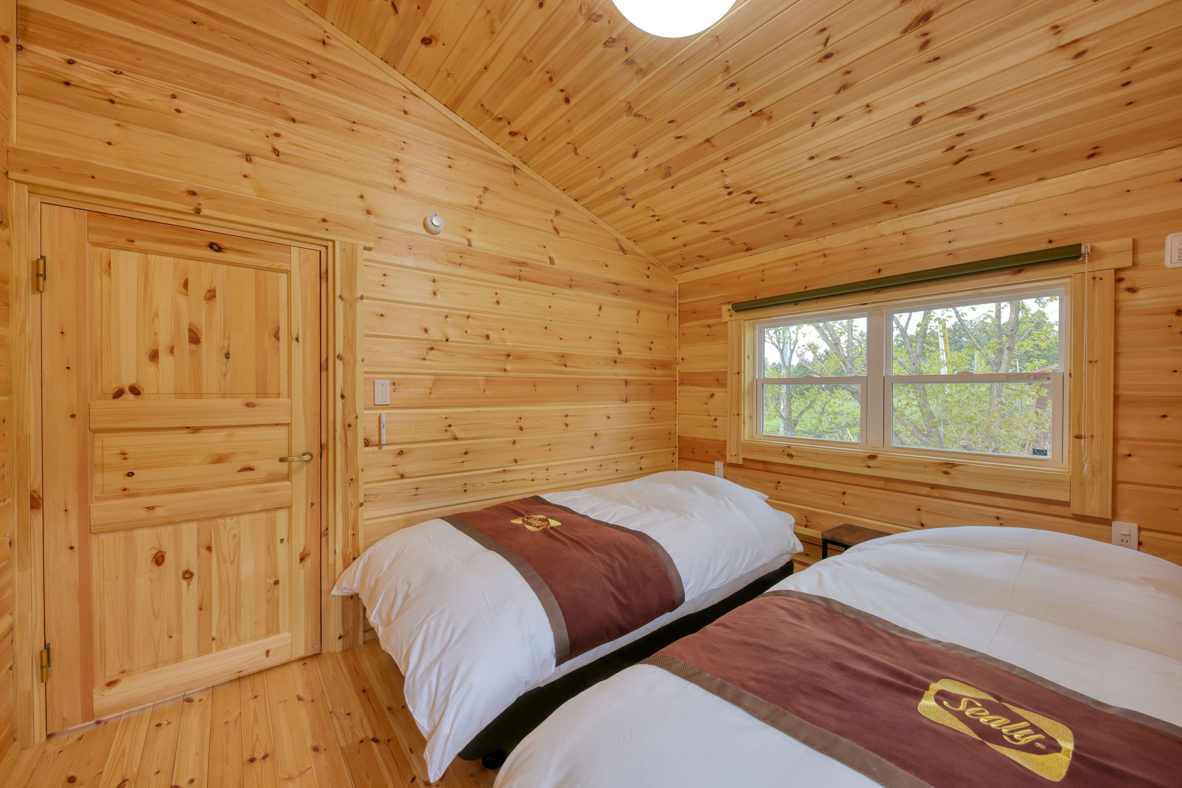 A wooden cabin room with two beds, a window, and a door.