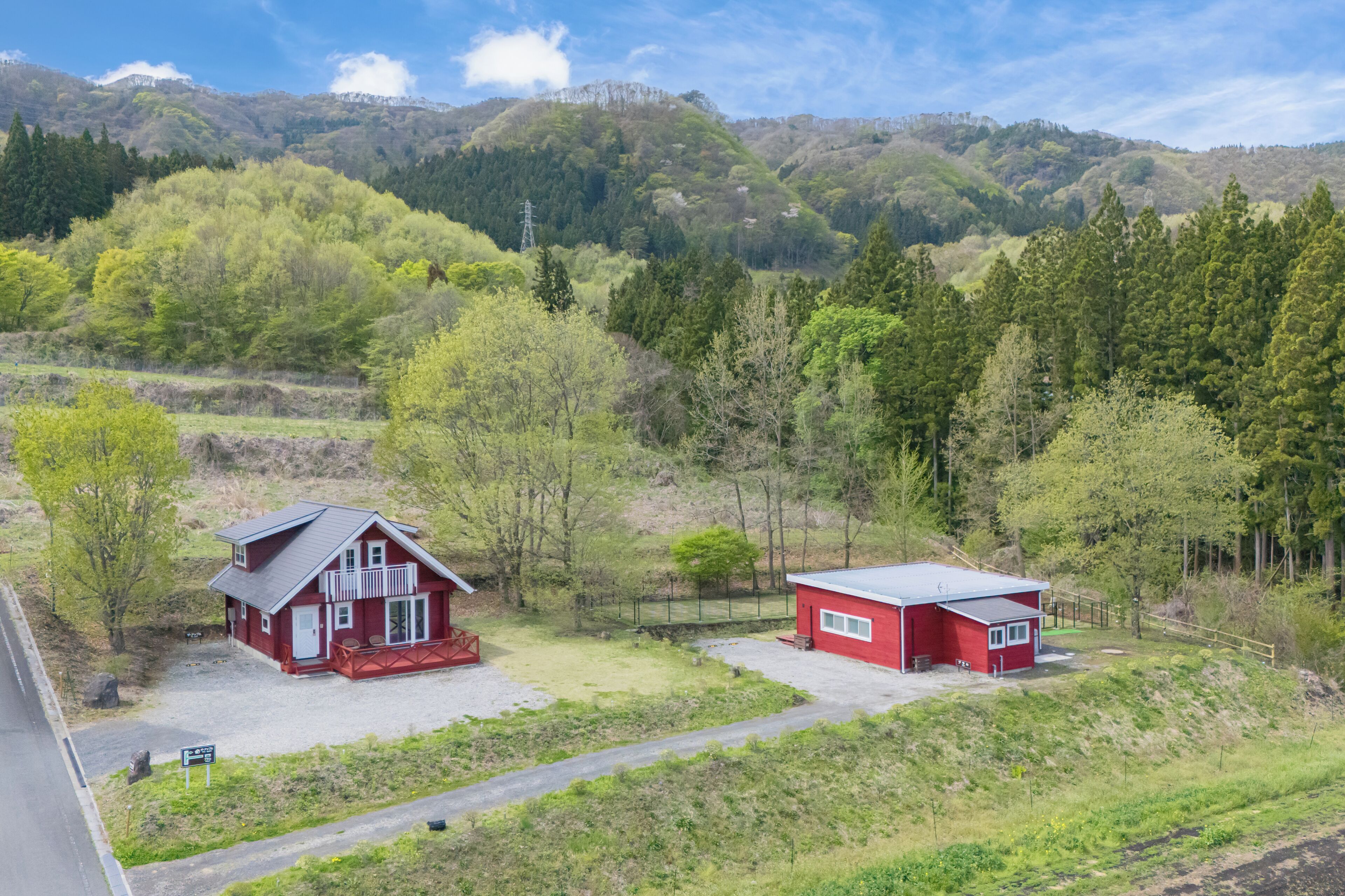 A red cabin with a balcony, a smaller red building, and a road in a mountainous area.