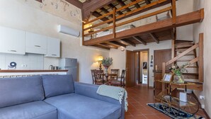 A living room with a sofa, a dining area with chairs, a staircase, and a kitchen with cabinets and appliances.