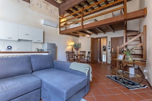 A living room with a sofa, a dining area with chairs, a staircase, and a kitchen with cabinets and appliances. - GuestHost - Renaissance Suite - Ferrara (Ferrara)