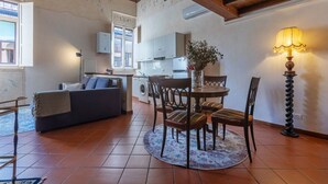 A cozy living room with a sofa, a dining table with chairs, a lamp, and a kitchen in the background.