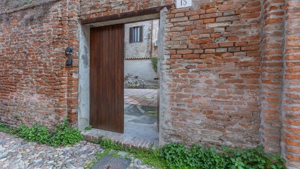 A brick building with a wooden door, a number '13' sign, and a bicycle in the background.