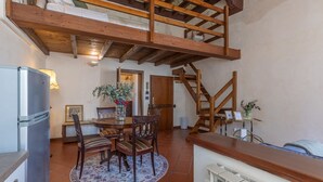 A rustic kitchen with a wooden ceiling, a dining area with a round table and chairs, and a staircase leading to an upper level.