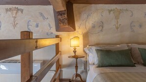 A bedroom with a wooden bed, a nightstand with a lamp, and a wall with floral patterns.