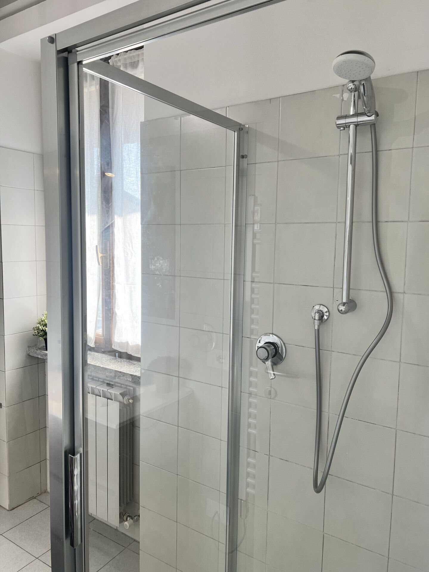 Ein modernes Badezimmer mit Duschkabine aus Glas, einer Handbrause und einem wandmontierten Wasserhahn.