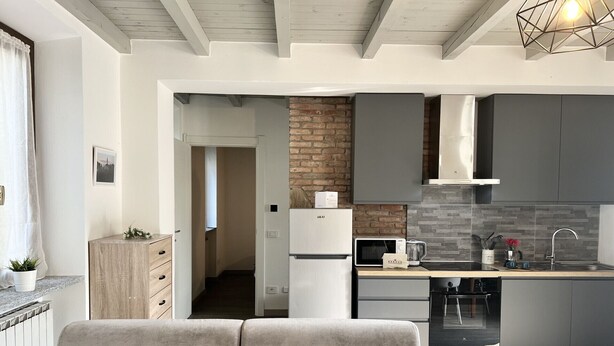 Una cocina moderna con microondas integrado, tostadora y hervidor, un sofá gris con cojín estampado y una pared de ladrillo decorativa.