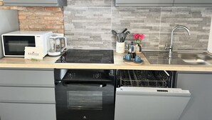 Una cocina moderna con microondas, hervidor y cafetera sobre la encimera, lavavajillas debajo y un lavabo con grifo.