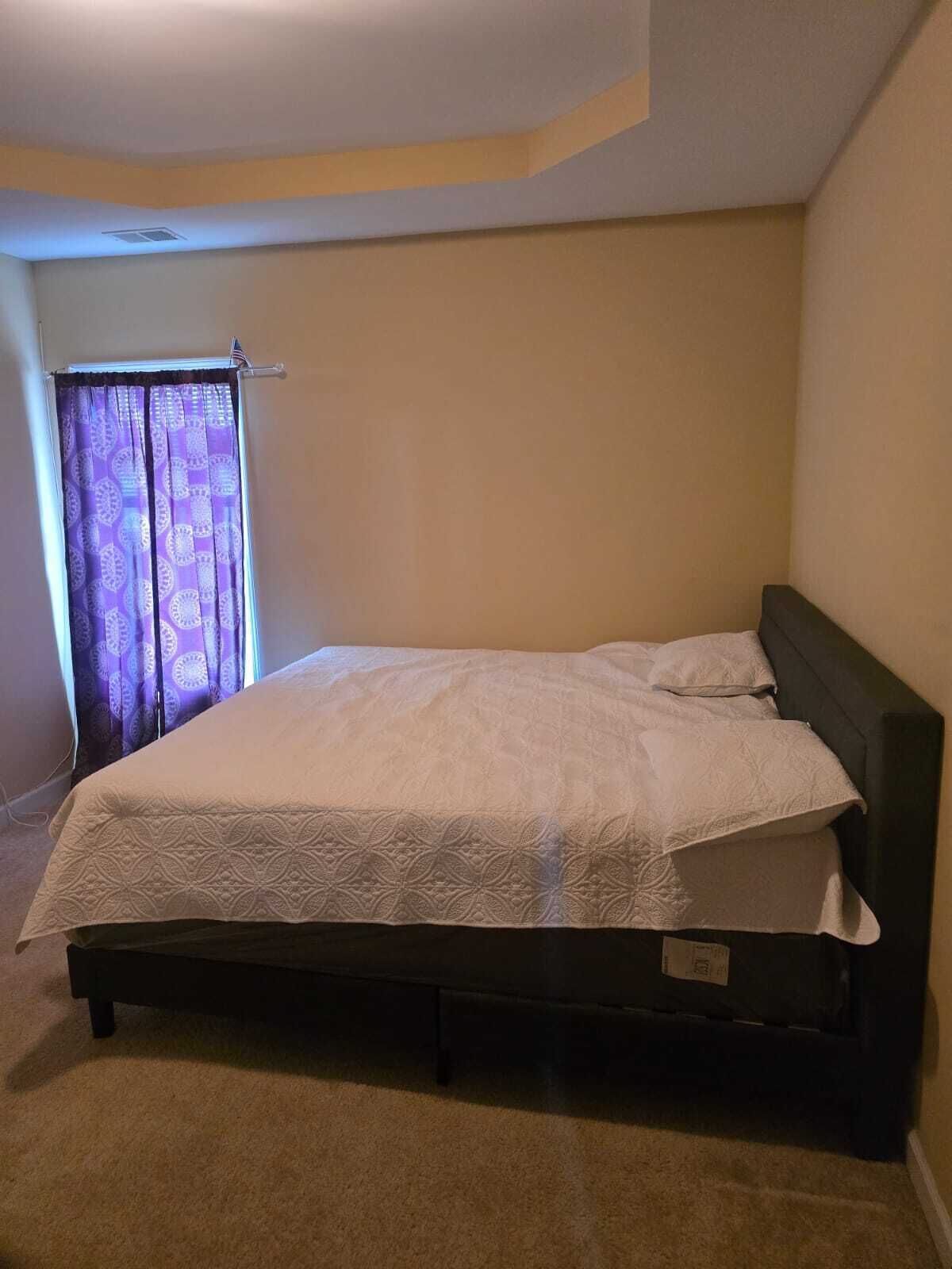 A single bed with a dark headboard in a room with beige walls and a carpeted floor.