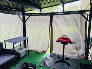 Un espacio exterior techado con una parrilla, asientos y una mesa.