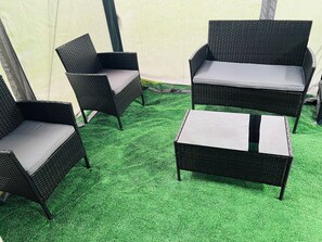 A set of outdoor wicker furniture with cushions, arranged on a green artificial turf surface.