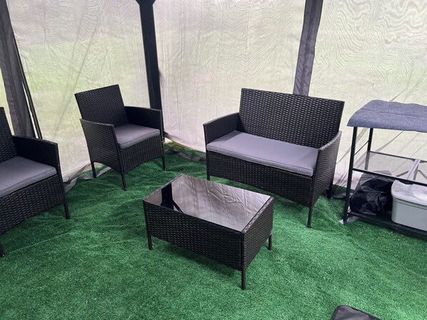 Un área de estar al aire libre con techo, muebles de mimbre y una pequeña mesa.