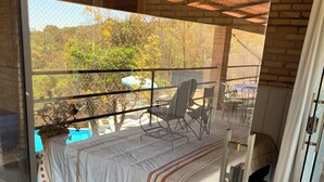 A balcony with a bed, chairs, and a view of the outdoors.