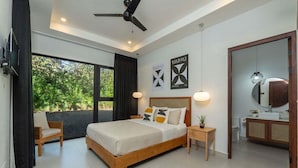 A modern bedroom with a large bed, a ceiling fan, a TV, and a view of greenery outside. - Villa in Exclusive Community 3-Min Drive to Beach w/ Private Pool, Sauna & Cold Plunge (Hacienda Pinilla)