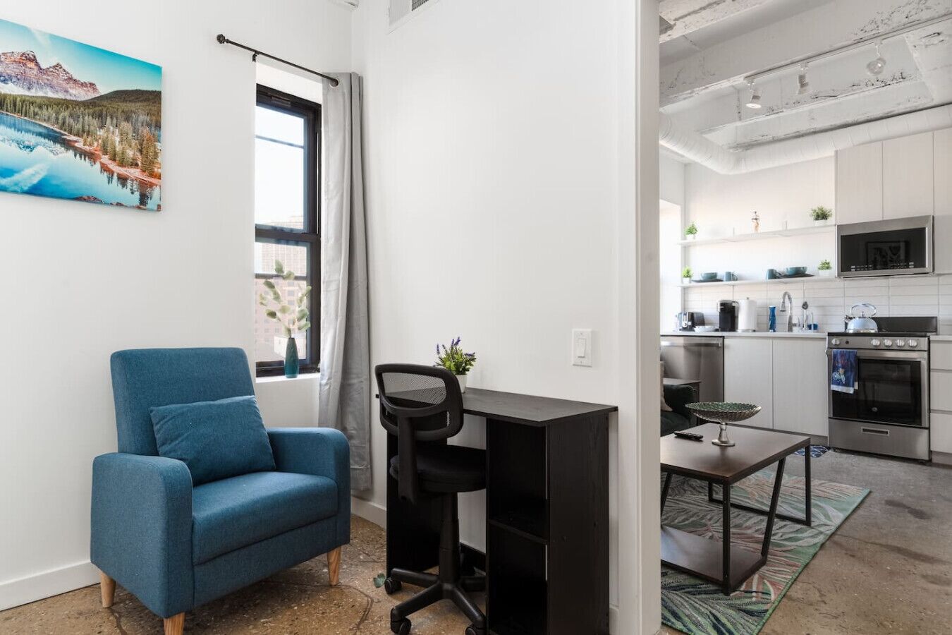 Un appartement moderne avec un fauteuil bleu, un bureau et un coin cuisine.