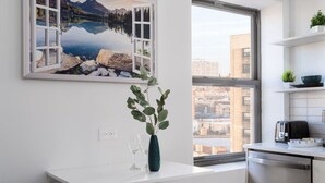 Una cucina moderna con un'ampia finestra, un piano di lavoro bianco e un dipinto raffigurante un paesaggio lacustre.