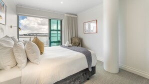 A hotel room with a large bed, a chair, a view of the sea, and a framed picture on the wall. - Waterfront Escape, Princes Wharf with Carpark (Auckland)