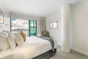 A hotel room with a large bed, a chair, a view of the sea, and a framed picture on the wall. - Waterfront Escape, Princes Wharf with Carpark (Auckland)