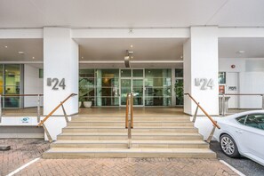 Ein moderner Gebäudeeingang mit Glastüren und einer Treppe, mit der Nummer 24 an der Wand.