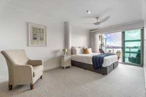 A bedroom with a bed, a chair, a nightstand, a ceiling fan, and a large window with a view of the water. - Waterfront Escape, Princes Wharf with Carpark (Auckland)