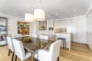 A modern kitchen with white cabinetry, a central island, pendant lights, and a dining area with a dark wood table and white chairs.
