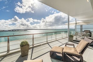 Un balcón con vista al mar, mobiliario exterior y una parrilla.
