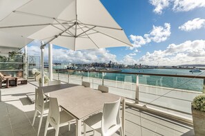 A terrace with a table and chairs, a large umbrella, and a view of a marina with boats and buildings. - Waterfront Escape, Princes Wharf with Carpark (Auckland)