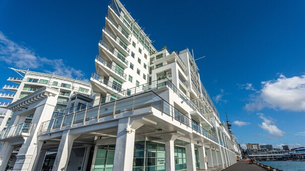 A modern multi-story hotel with a glass facade, outdoor seating area, and a view of the waterfront. - Waterfront Escape, Princes Wharf with Carpark (Auckland)