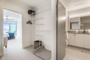 Ein modernes Hotelzimmer mit begehbarem Kleiderschrank, einem Balkon mit Bett und einem Badezimmer mit großem Spiegel und Waschbecken.