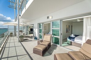 A balcony with wicker furniture, a sliding glass door leading to a bedroom, and a view of the sea.