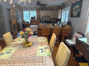A dining area with a table set for six, a vase with flowers, and a fruit bowl.
