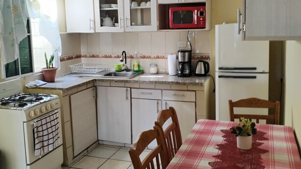 A compact kitchen with white cabinets, a red microwave, a gas stove, and a dining table with a plaid tablecloth.