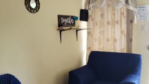 A room with a blue sofa, a small table with a sign, a mirror, and a curtain with a floral pattern.