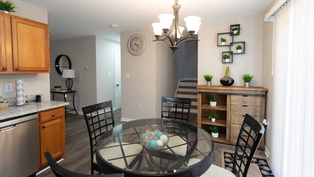 A modern dining area with a glass table, black chairs, wooden cabinets, and a chandelier.