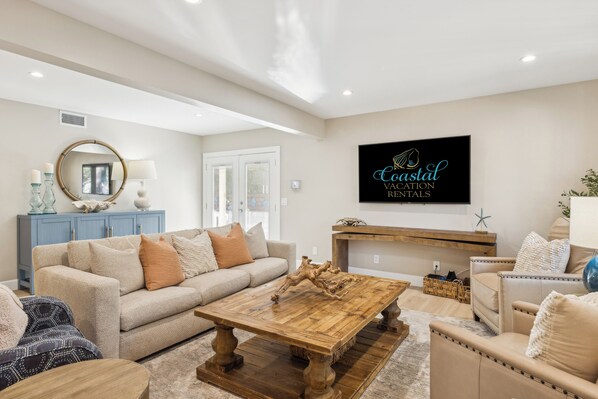 Un salon avec un canapé beige, une table basse en bois et un téléviseur fixé au mur qui affiche des annonces de «
locations de vacances en bord de mer
».