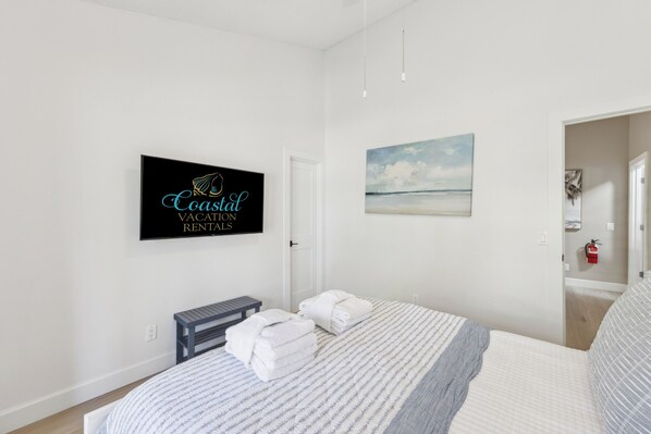 A bedroom with a bed, a sign reading "Coastal Vacation Rentals," a painting of a beach, and a fire extinguisher on the wall. - 4-Bedroom beach house, steps away from Coligny Plaza (Hilton Head Island)
