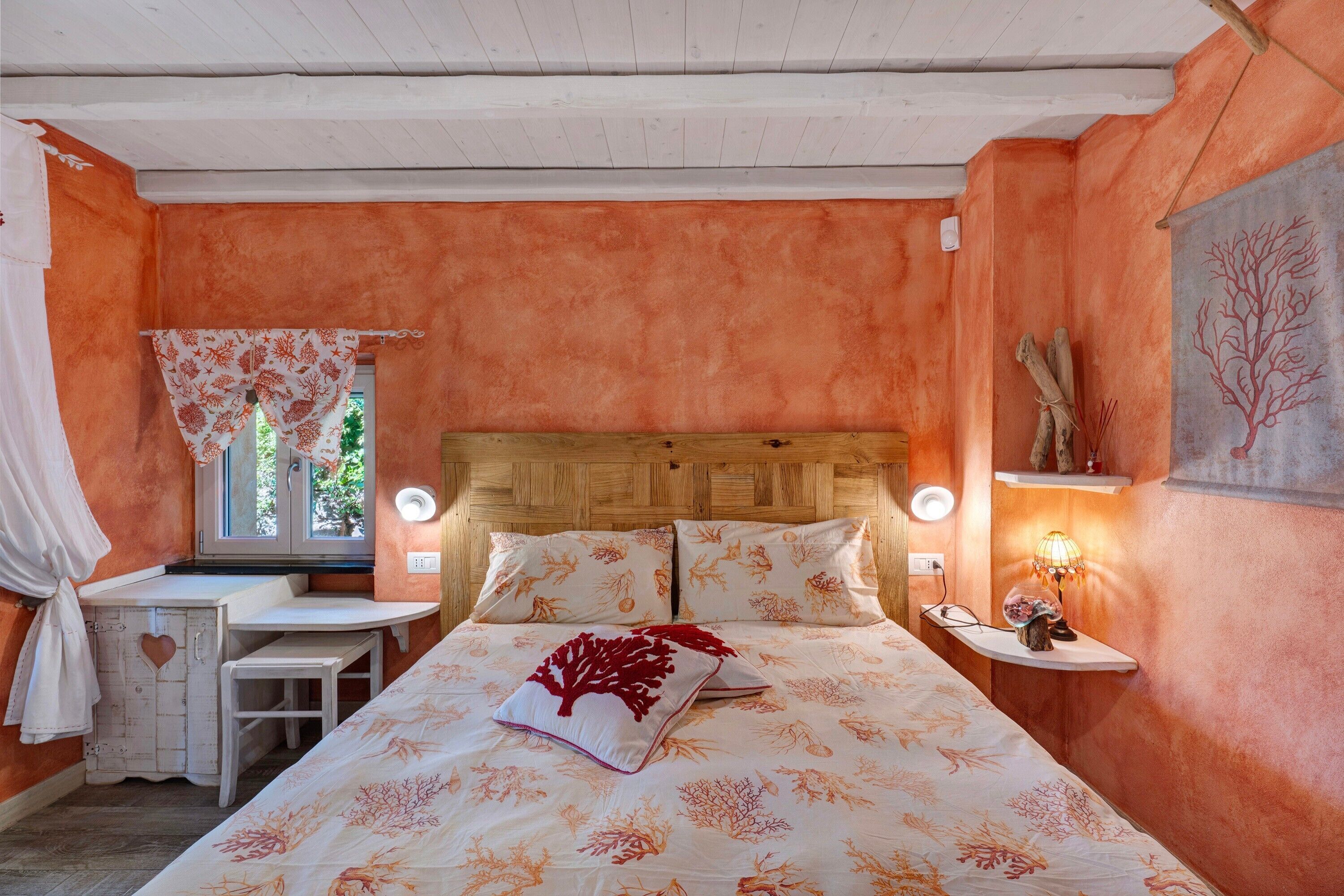 A bedroom with a wooden headboard, a bedside table, a nightstand with a lamp, and a window with curtains.